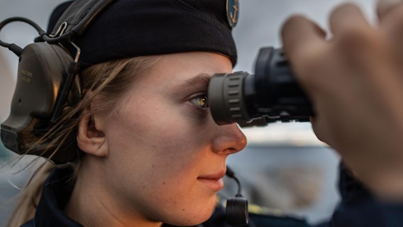 Kvinnlig militär spanar genom kikare långt bort ut bilden