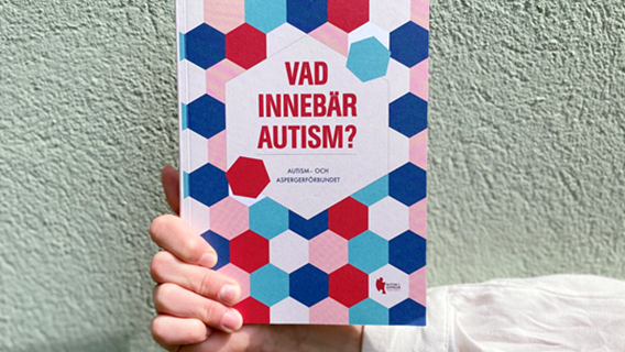 En hand visar upp framsidan av boken Vad innebär autism