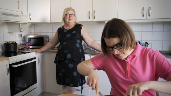 Jenny äter vid köksbordet och mamma Birgitta står bakom vid köksbänken