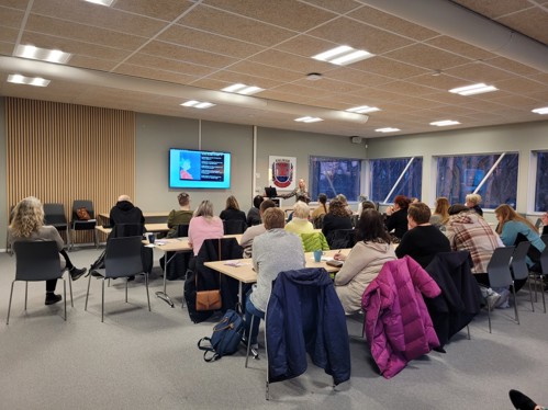 Föreläsning med åhörare i ett konferensrum. Föreläsaren står vid podiumet och atmosfären är fokuserad.
