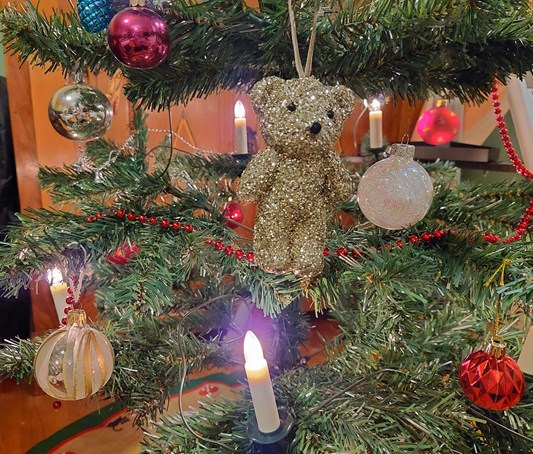 Julgran med ljus och dekorationer, t ex en glittrande nalle